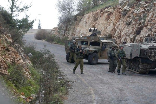 Israeli soldiers walk near military vehicles near Israel's border with Lebanon