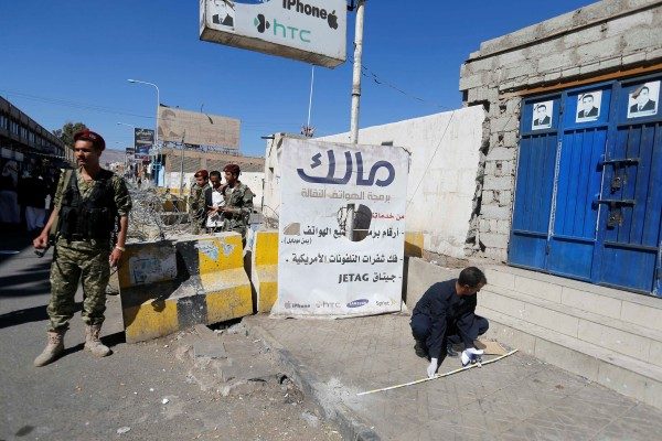 Houthi militiaman stands guard as a forensic expert inspects the scene of a blast near the republican palace in Sanaa