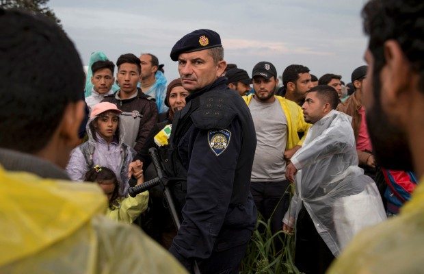 Police officer maintains order as migrants wait in field after crossing border near Tovarnik
