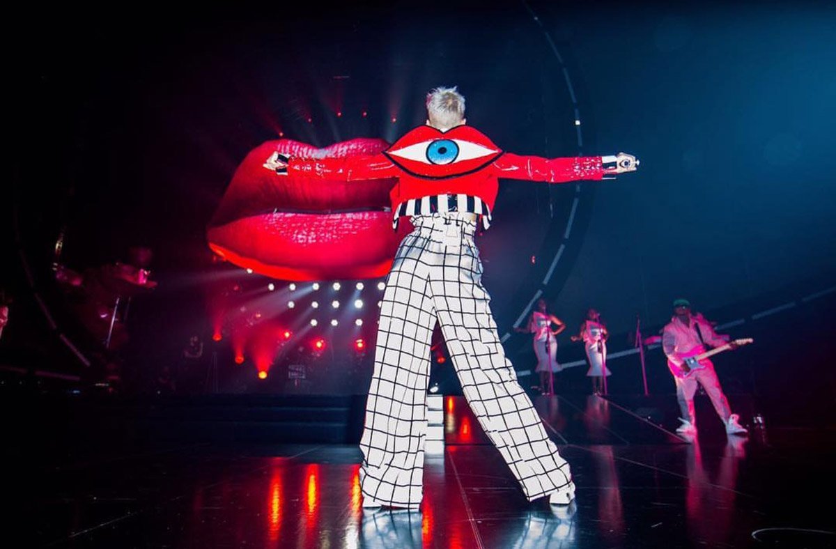 Katy Perry, Johnny Wujek imzalı, sırtında büyük bir dudak ve göz görünümlü kırmızı ceketini yüksek bel bir palazzo pantolon ile kombinlemiş.